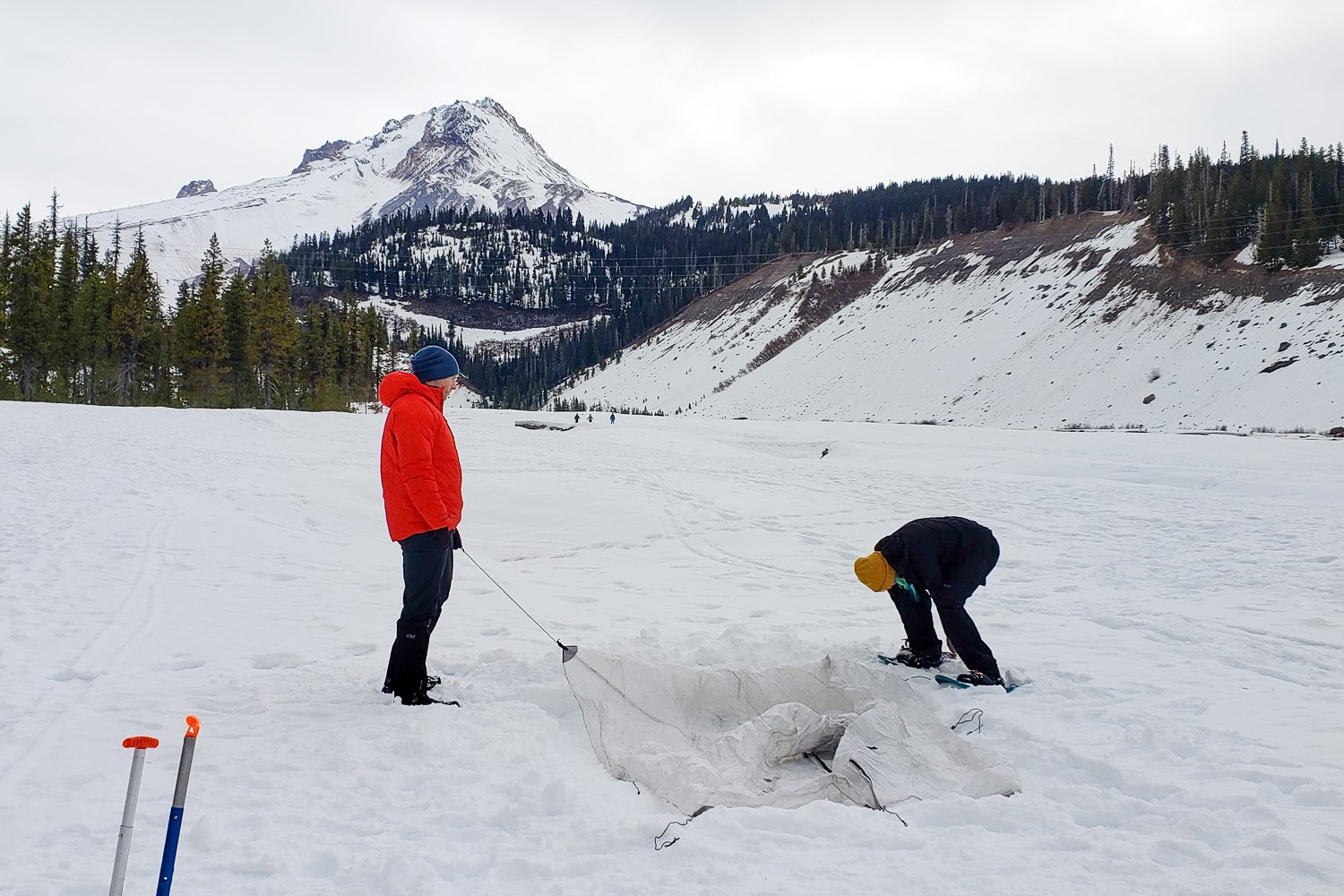 Two hikers setting up a tent in the snow with a mountain in the background