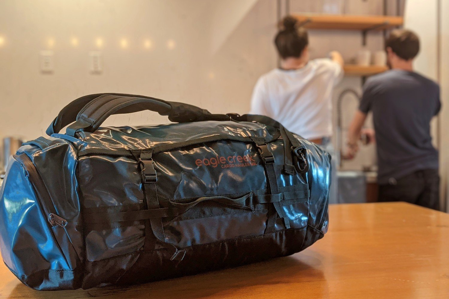 The Eagle Creek Cargo hauler duffel sitting on a counter of a kitchen with two people in the background