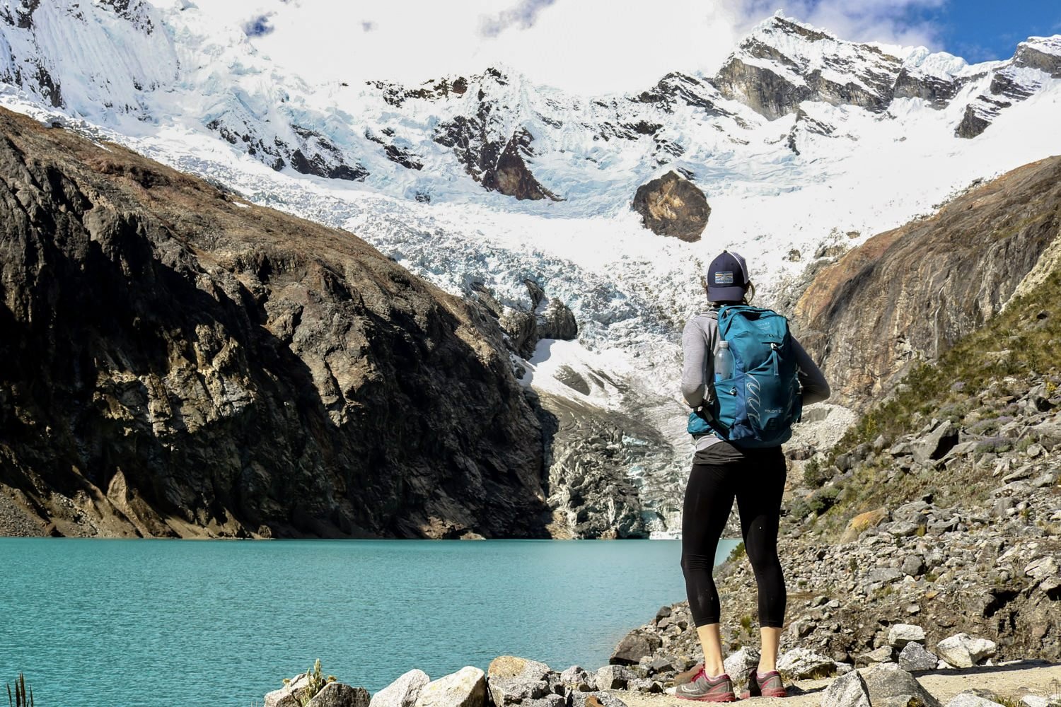 A hiker looking up at a glacier near a turquoise lake wearing the Osprey Tempest 20 backpack