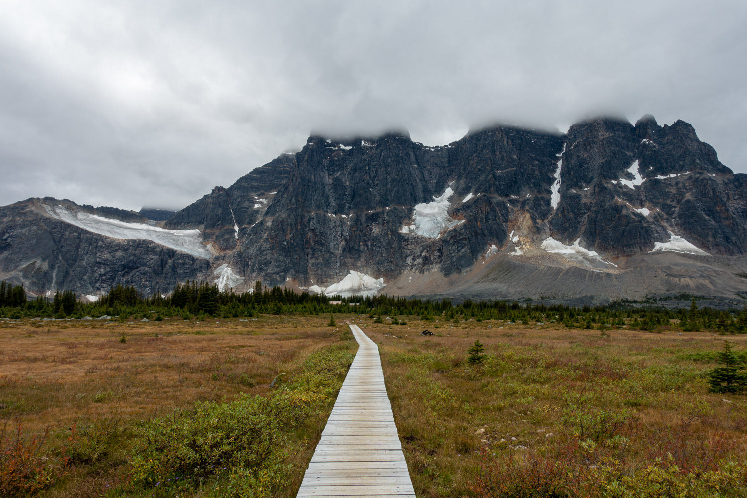 A boardwalk trail leading towards steep, glaciated mountains.