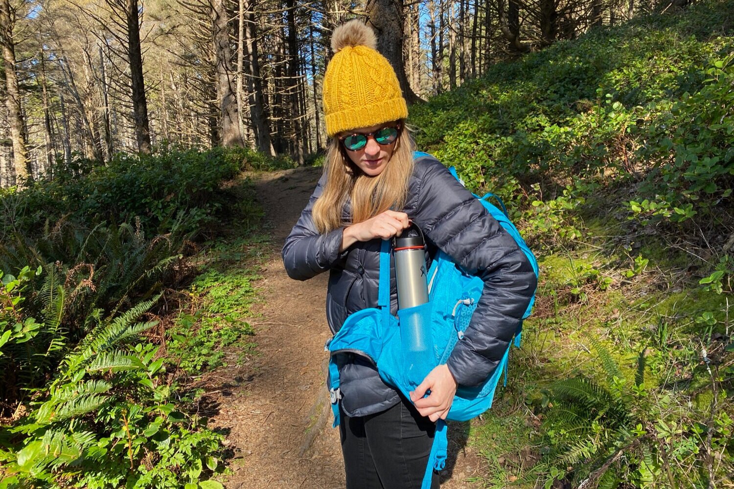 A hiker with a yellow beanie hat putting a Hydro Flask into the side pocket of the Gregory Juno 24