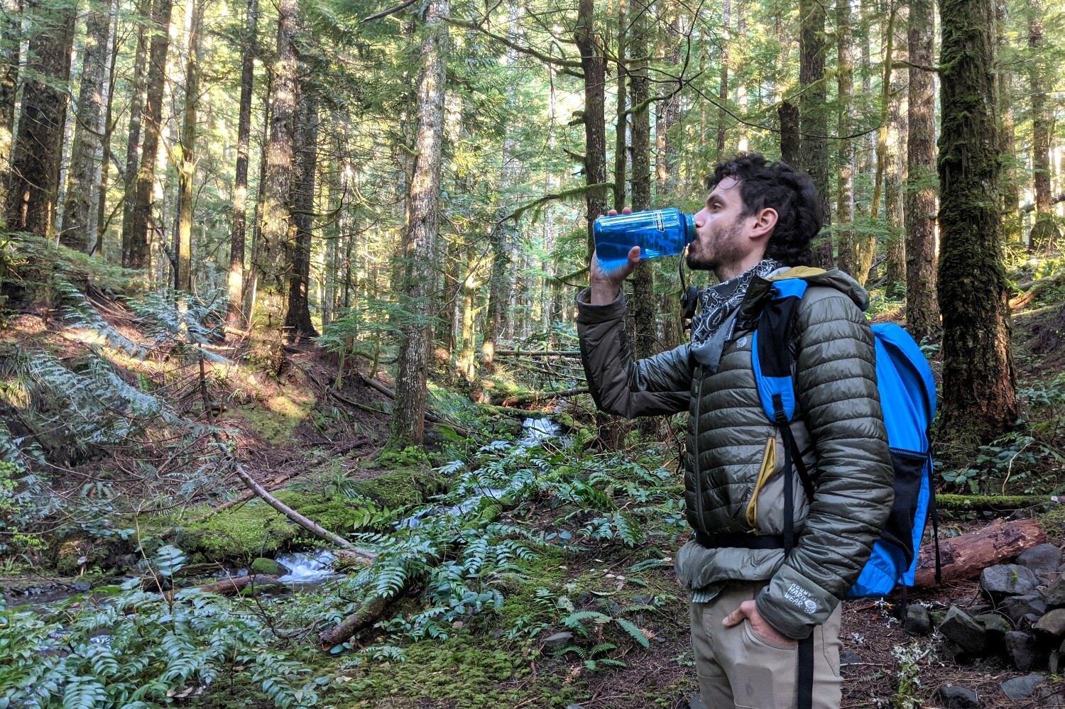 A hiker standing in a forest drinking water from a Nalgene - theyre wearing the Six Moon Designs Wyeast daypack