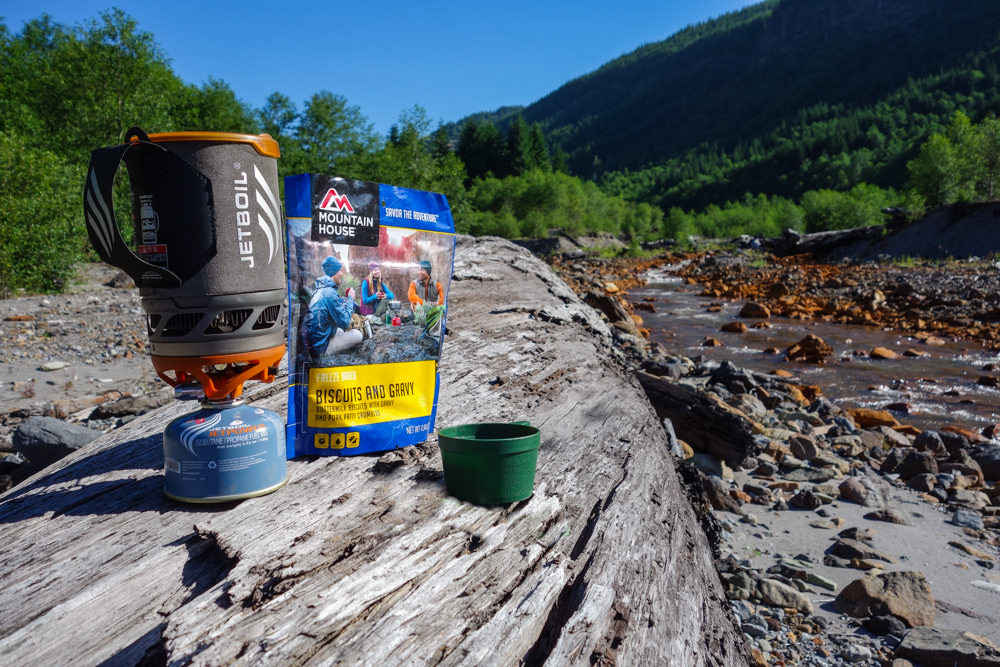 A Jetboil Flash Backpacking Stove with the Mountain House Biscuits and Gravy Dehydrated Meal on a log.