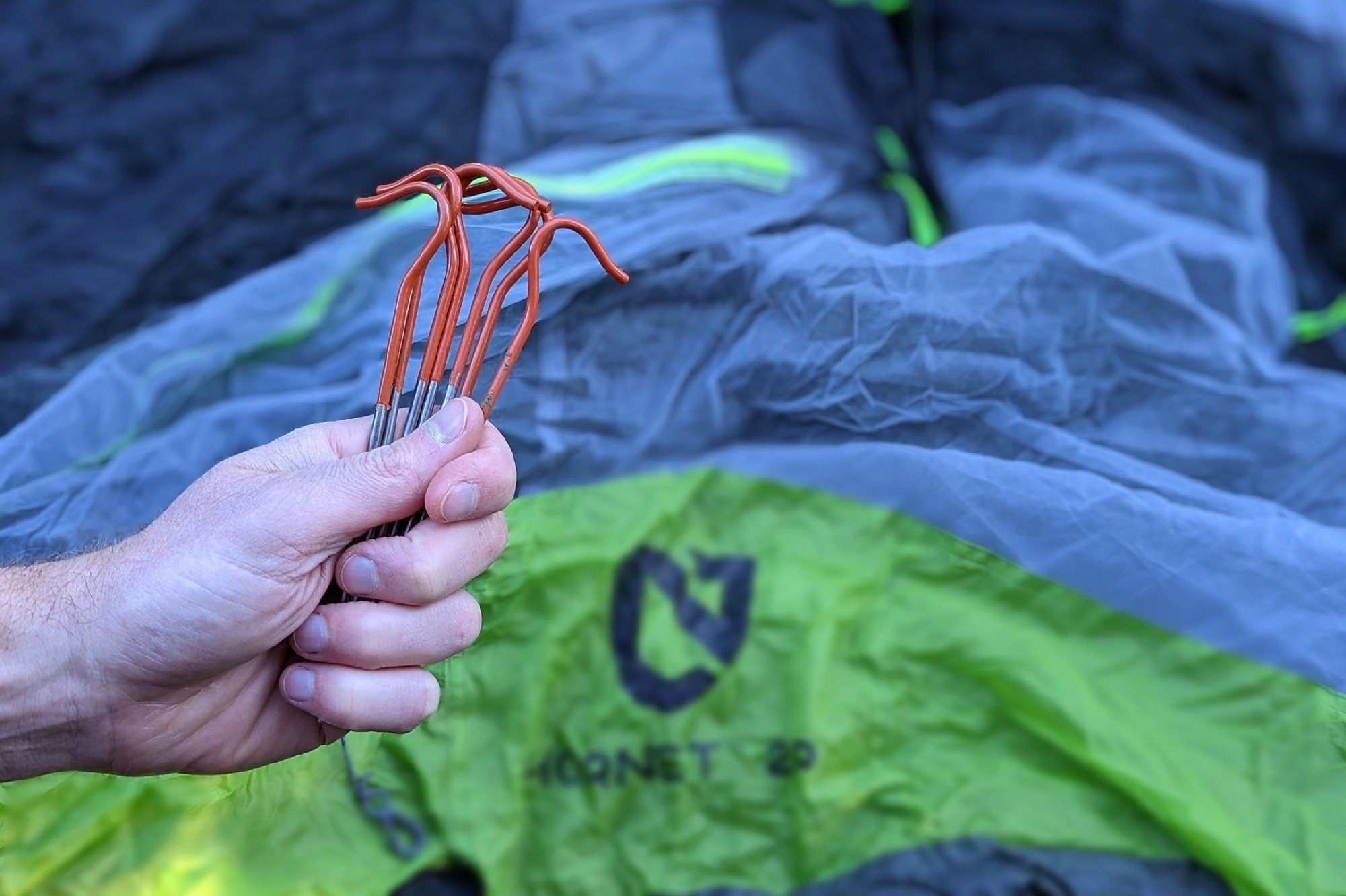 Someone holding a set of Vargo Titanium tent stakes in front of a tent