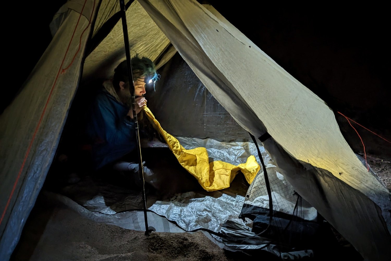 A hiker sitting in a tent blowing up a sleeping pad. It's night time and the hiker has a Nitecore NU25 UL headlamp on to light the interior of the tent