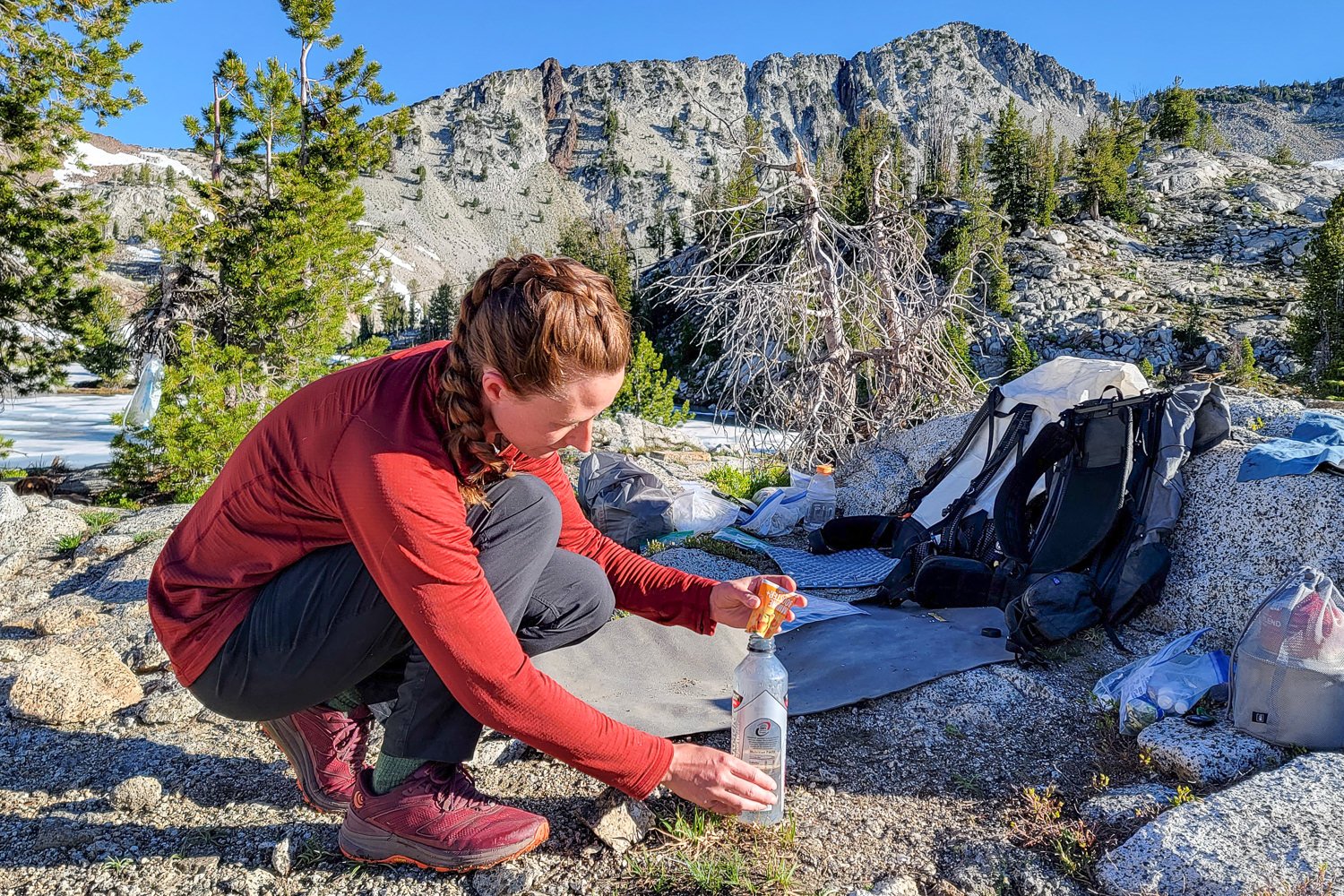 A hiker pouring electrolyte mix into a water bottle with mountains in the background