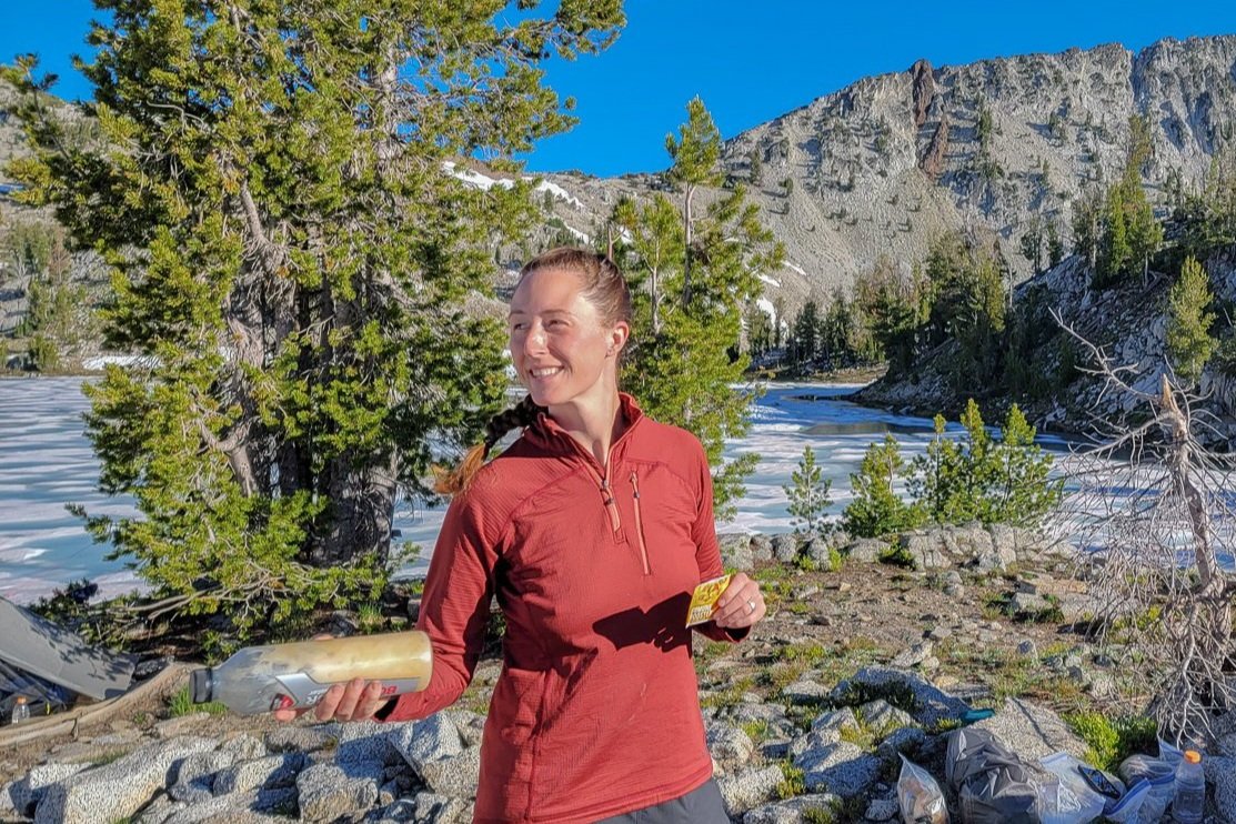 A hiker shaking a water bottle with Dr Price Immune Booster electrolyte mix in it