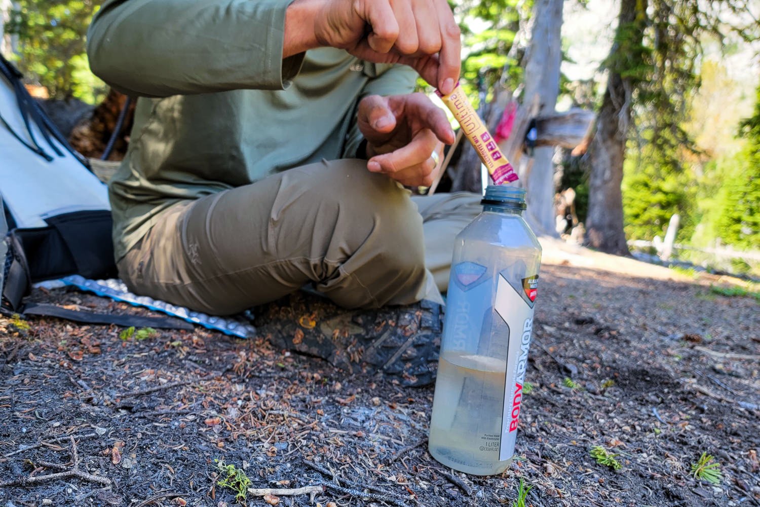 A hiker pouring Ultima Replenisher electrolyte mix into a water bottle