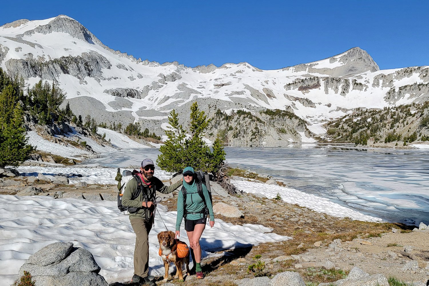A couple and their dog in front of a glacial lake in the Baleaf Triumph & OR Echo sun shirts