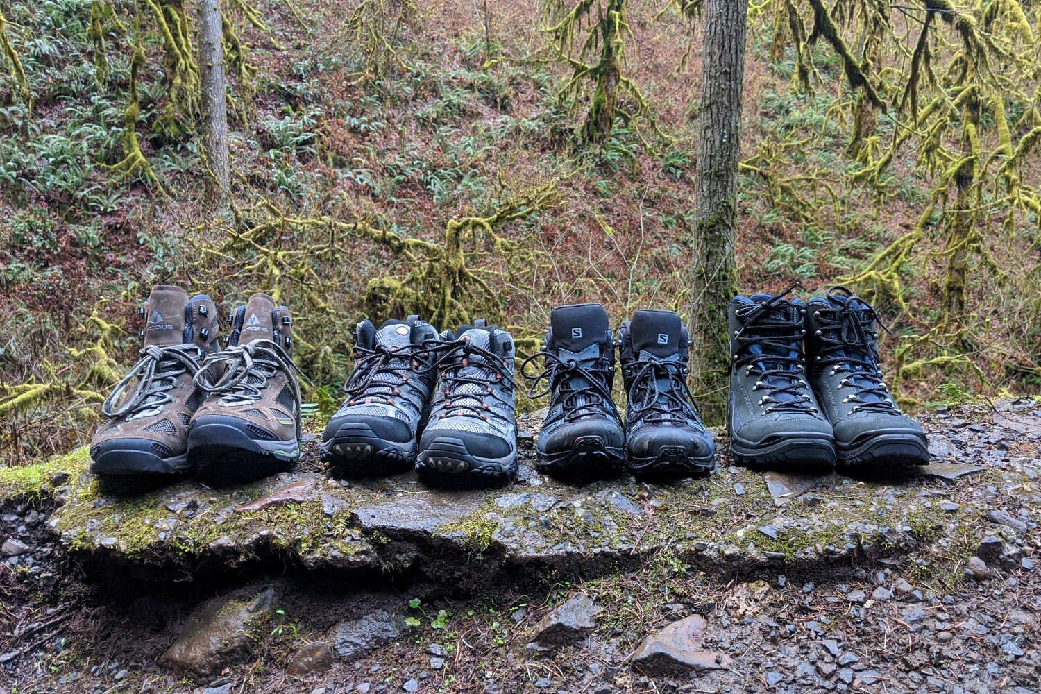 Four pairs of hiking boots side-by-side on a rock for comparison.