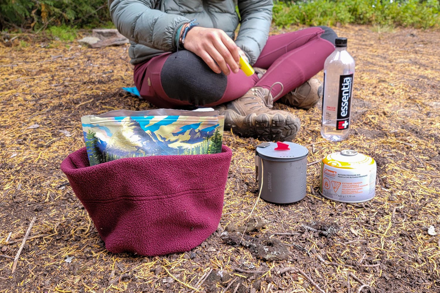 A backpacker using a fleece hat as a coozie for freeze-dried backpacking meal