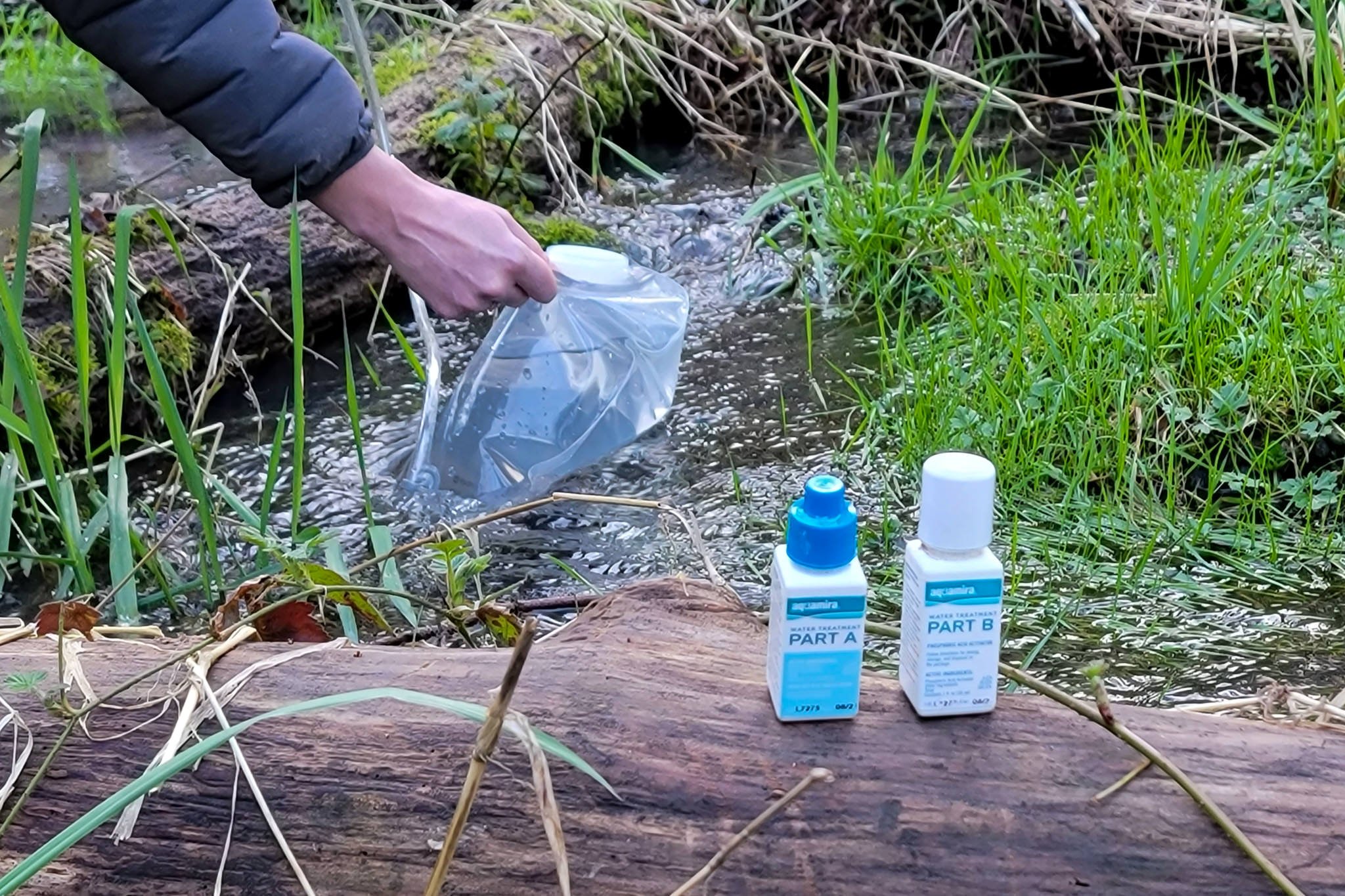 A hiker refilling their hydration bladder in a creek and using Chlorine Dioxide Drops for purification