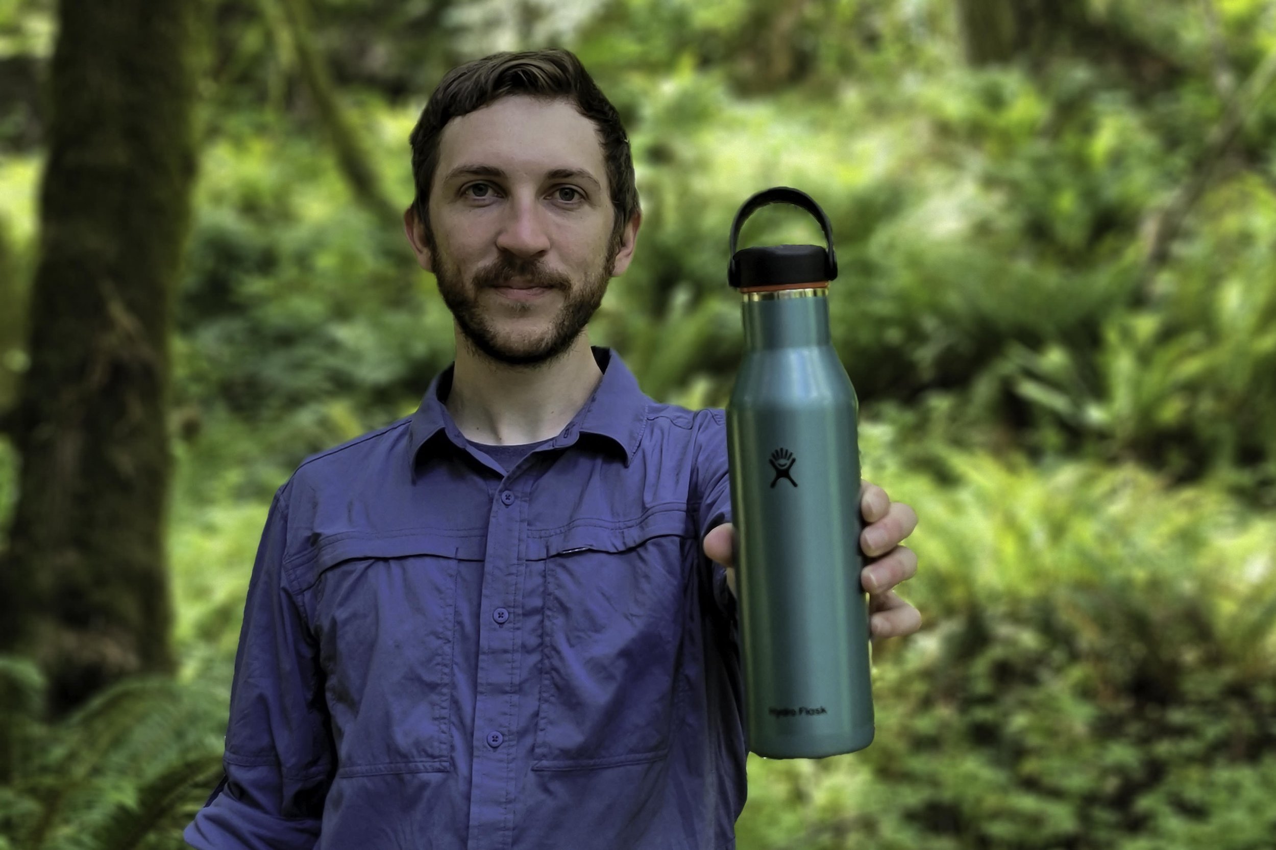 A person holding out a Hydro Flask Lightweight Insulated Bottle in a forest