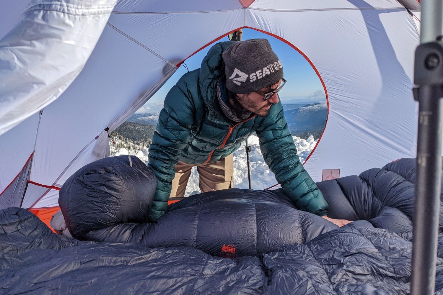 A hiker laying out the REI Magma 16 sleeping bag in a tent on a winter trip