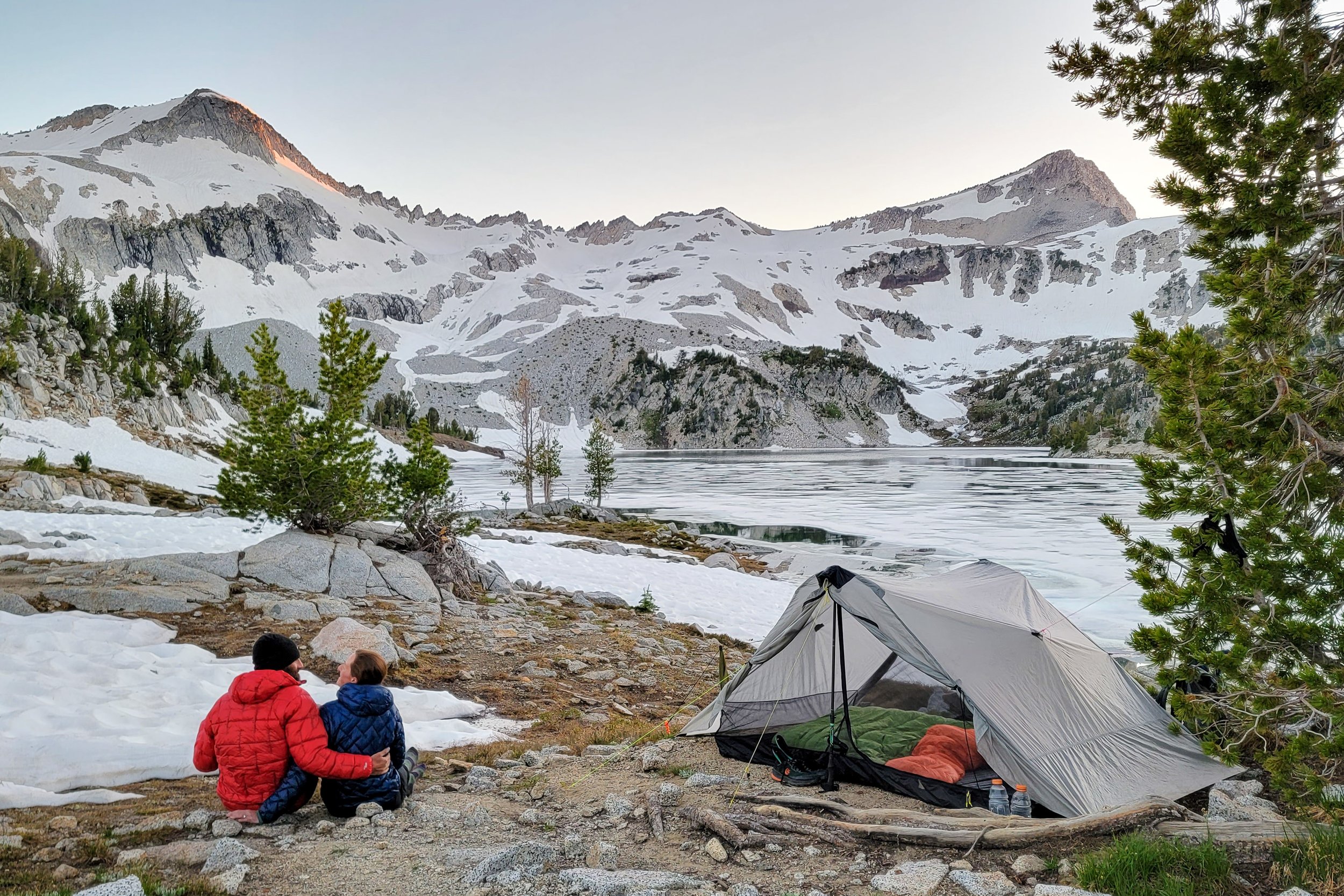 A couple sitting next to the Six Moon Designs Lunar Duo tent surrounded by snowy mountains