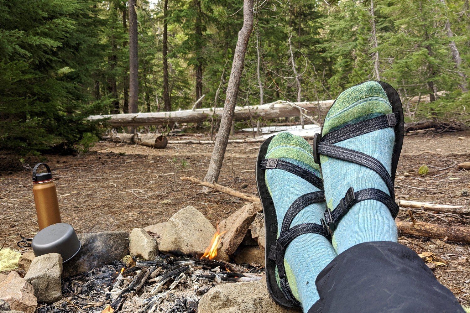 Person's feet in a pair of socks by an extinguished campfire