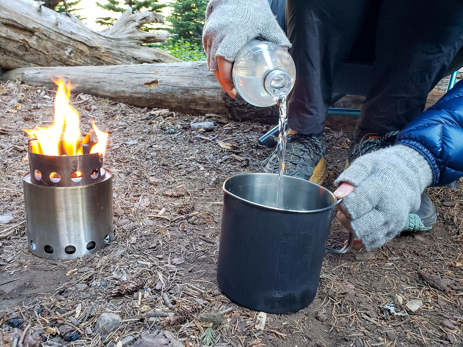 Pouring water into a pot next to the flaming Solo Stove Lite backpacking stove.