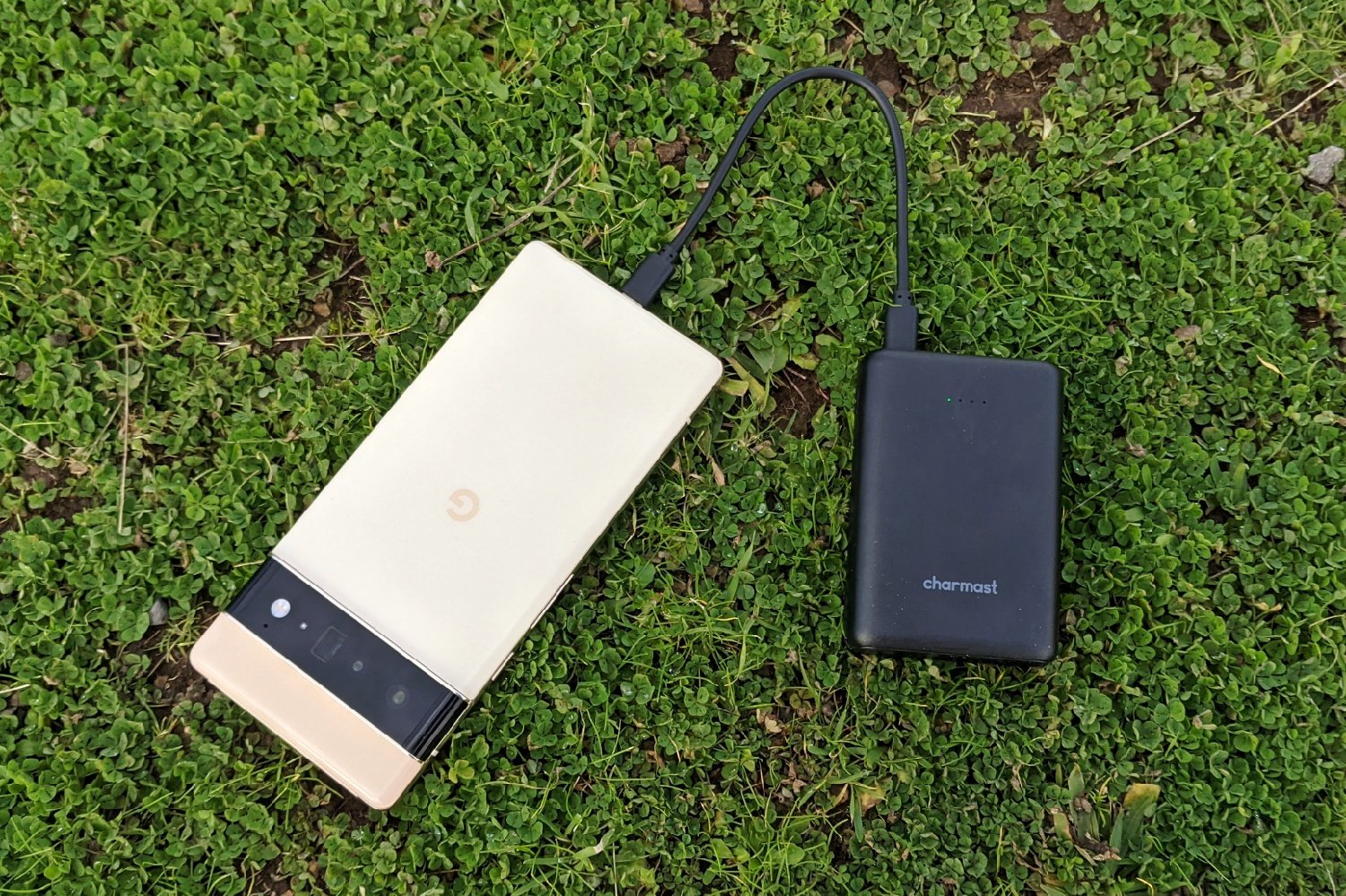 The Charmast 10000 Mini Power Bank plugged into a phone sitting on some grass