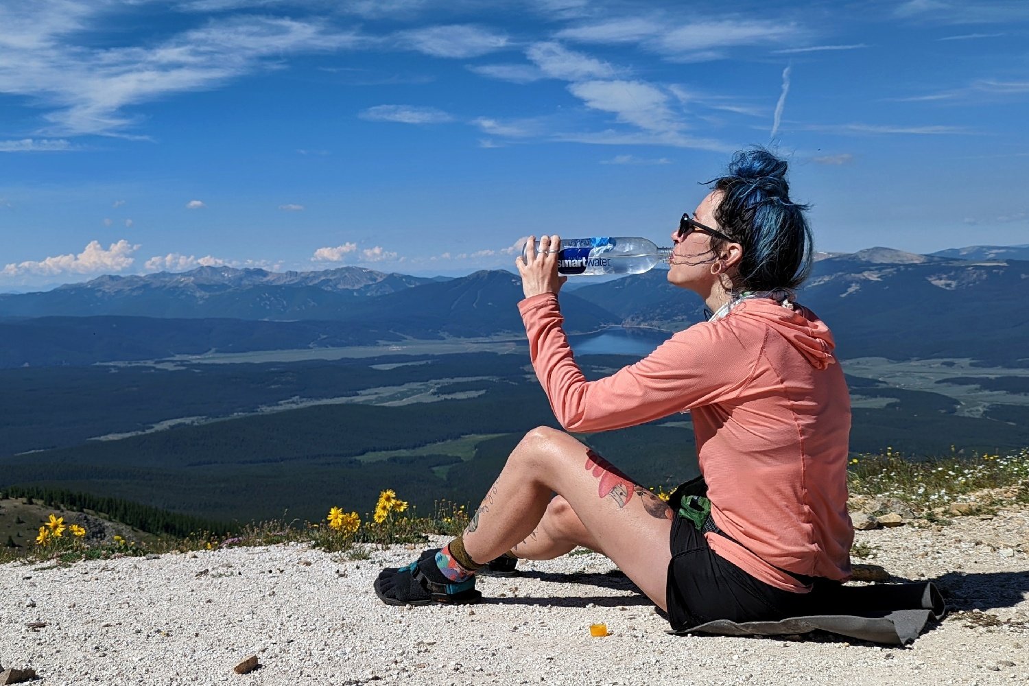 A hiker sitting on the ground drinking from a water bottle on a high elevation mountain pass