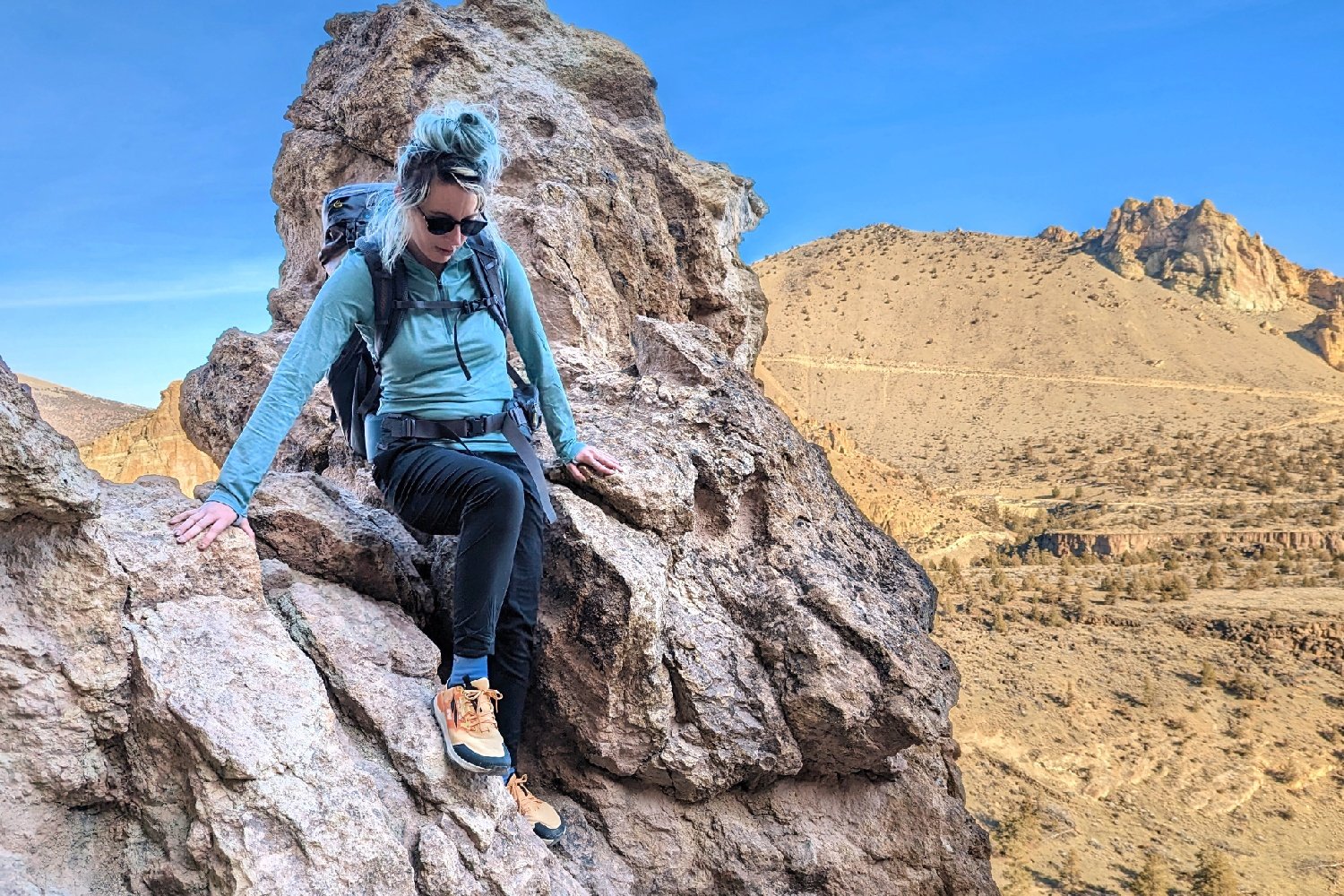 A hiker climbing down some rocks in a desert landscape wearing the REI Midweight Half Zip Base Layer