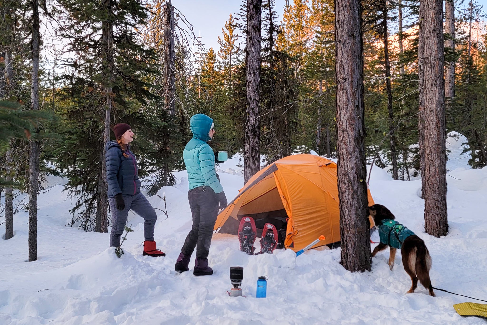 Two women wearing down pants in a snowy winter camping scene
