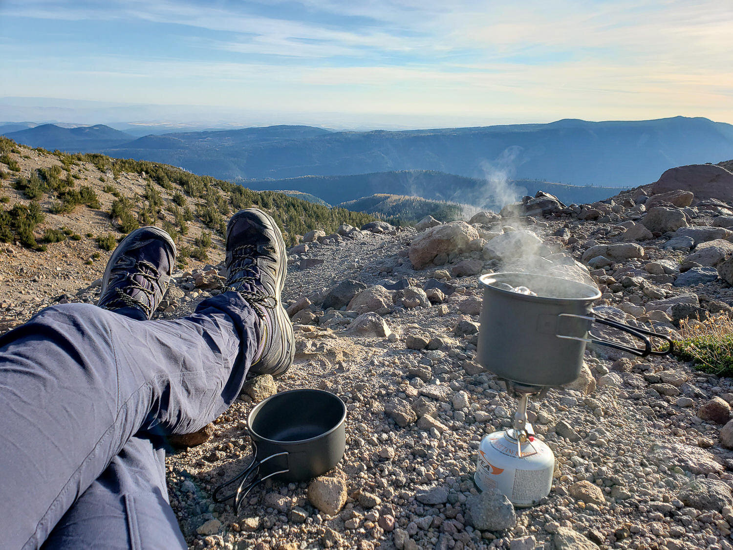 Water steaming over a backpacking stove with a view of the mountains in the background.