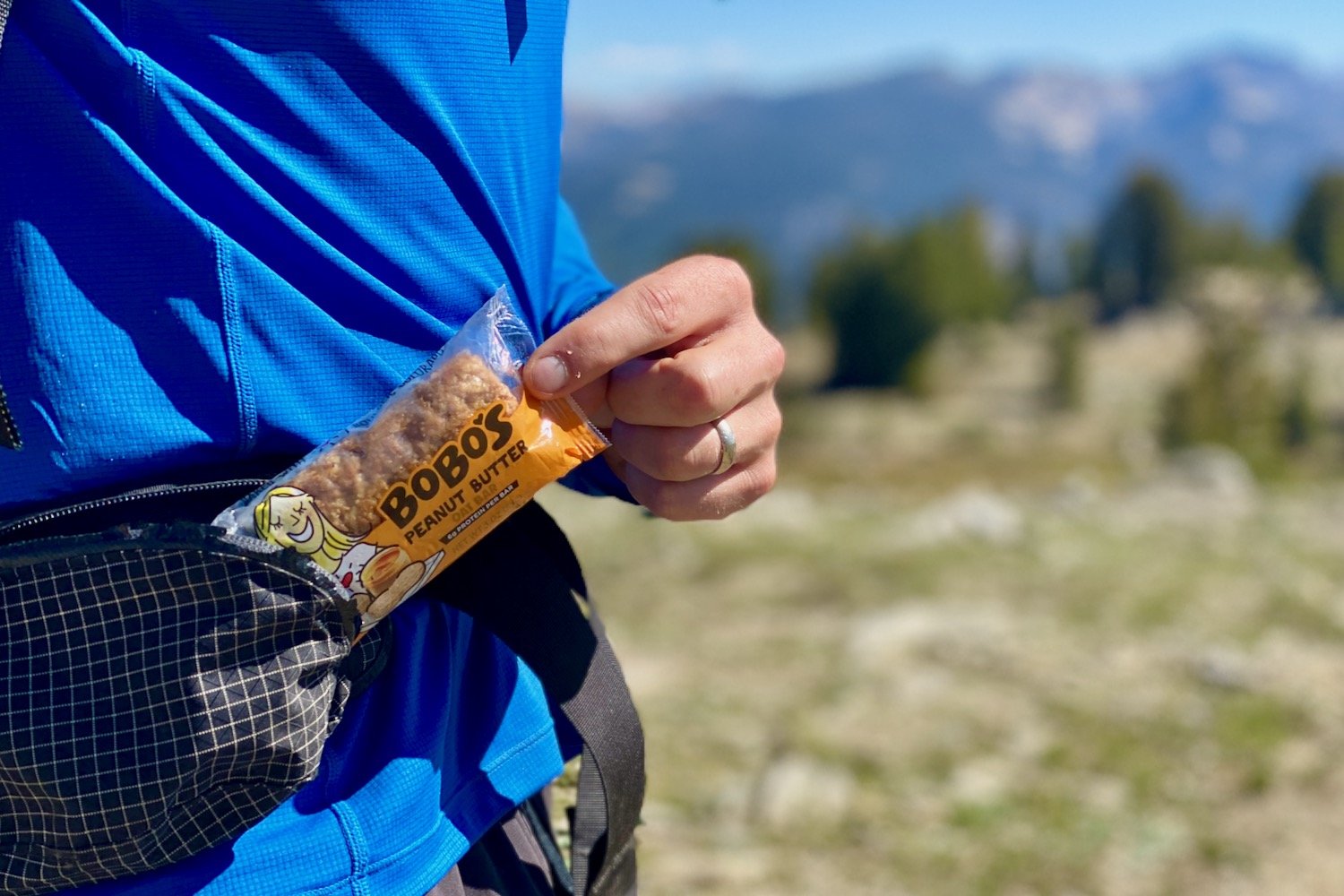 Closeup of a backpacker taking a Bobo's Energy Bar out of their hip belt pocket